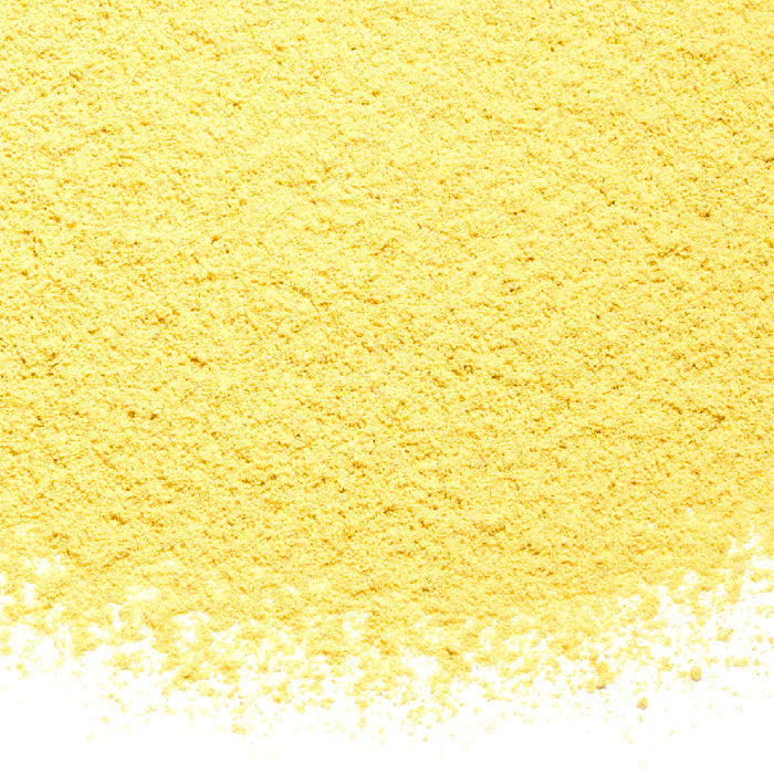 A close-up of Ginger Powder Organic by Whole Spice Inc. shows a scattered pile of fine yellow powder spread unevenly over a white background.