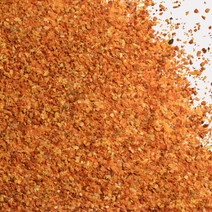 A close-up of Whole Spice Inc. Grapefruit Peel, an orange and yellow crushed seasoning with citrus notes, scattered on a white background.