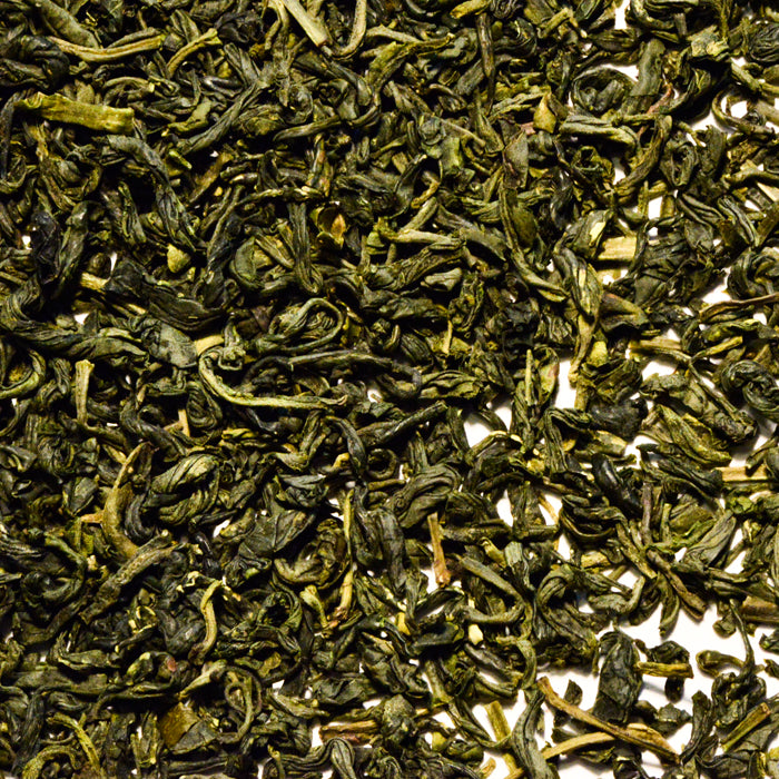 A close-up of Whole Spice Inc.'s Yunwu Cloud Mist Green Tea shows twisted, dry green leaves densely scattered on a light background.