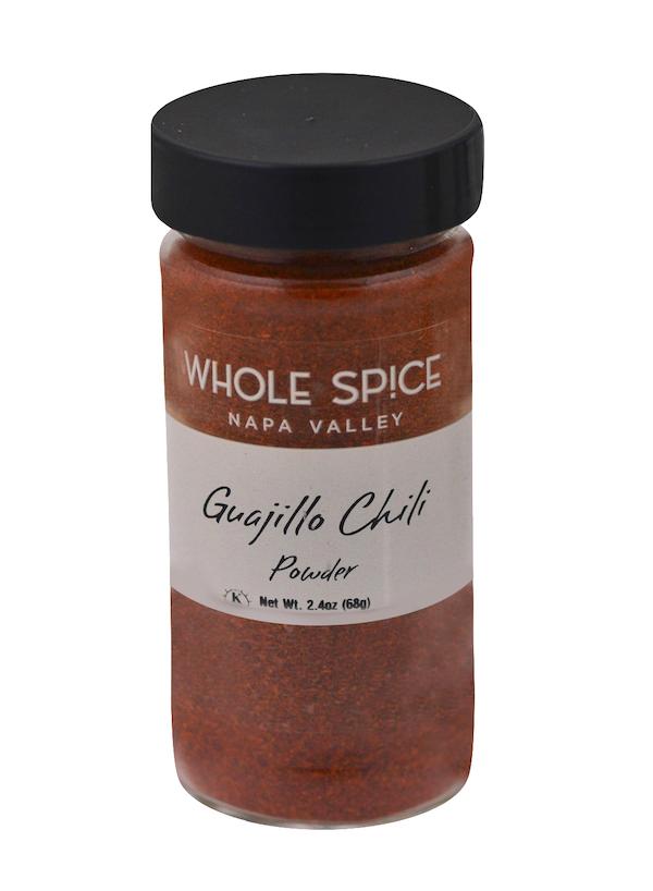A clear spice jar with a black lid labeled Whole Spice Inc. Guajillo Chili Powder contains rich red Mexican chili pepper powder, ideal for adding depth to mole sauce. Net weight: 2.4 oz (68g).