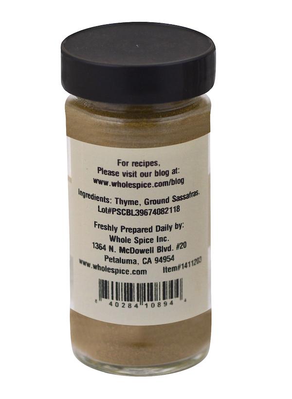 A clear spice jar with a black lid is shown from the back, featuring a Whole Spice Inc. Gumbo Filé label with ingredients like thyme and ground sassafras, company details, and a barcode at the bottom.