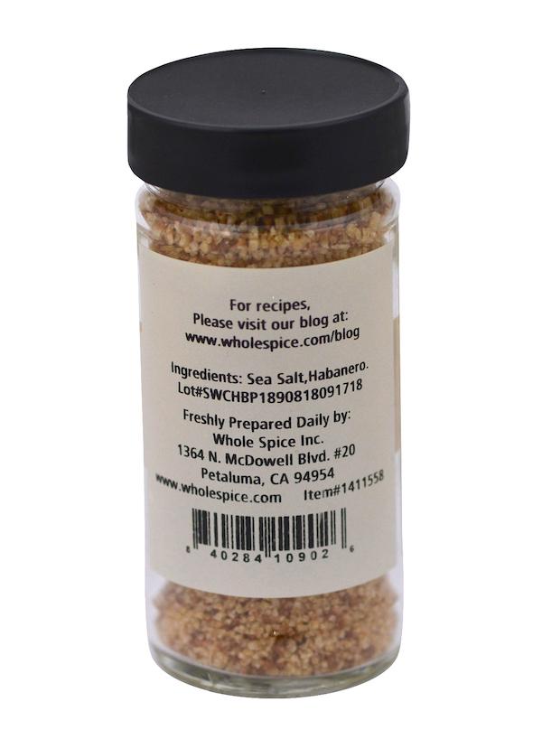 A clear spice jar with a black lid holds Whole Spice Inc. Habanero Salt, a coarse orange-brown blend. The label lists sea salt and habanero, the manufacturer's address, and a website for spicy seasoning recipes.