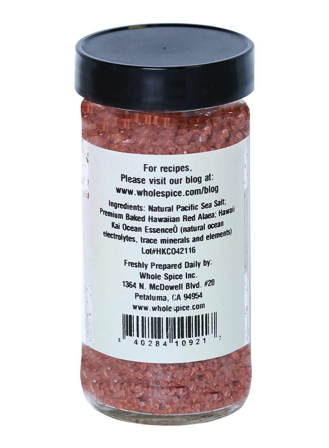 A clear spice jar with a black lid from Whole Spice Inc. contains Hawaiian Red Gold Sea Salt, made with Hawaiian sea salt and Alaea clay. The back label displays ingredients, company info, and a barcode at the bottom.