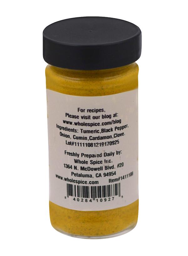 A clear spice jar with a black lid holds Hawaj Soup Blend by Whole Spice Inc.—a yellow powder of turmeric, black pepper, onion, cumin, cardamom, and clove. The label includes classic Yemeni blend details plus company address and contact info.