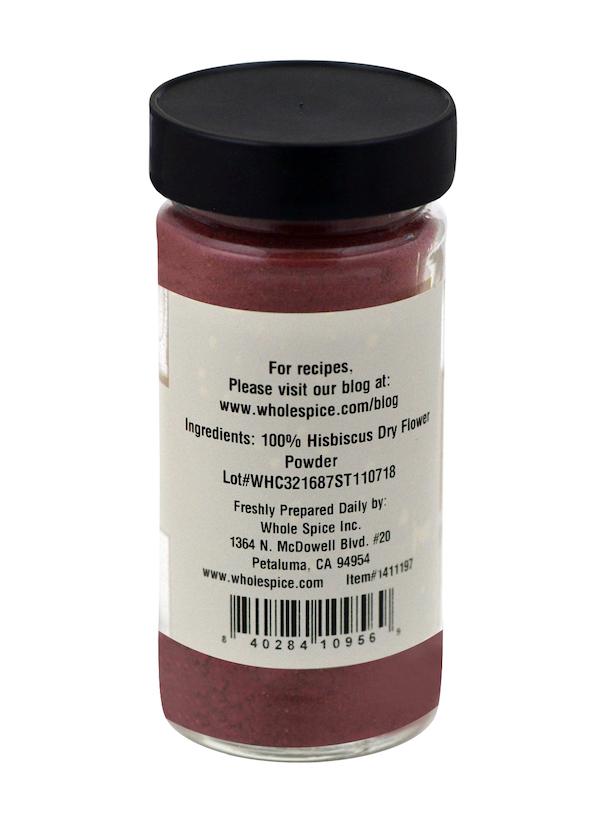 A clear spice jar from Whole Spice Inc. contains Hibiscus Powder labeled as 100% Dry Flower Powder, with a back label listing ingredients, a blog link, lot number, and contact details—ideal for making hibiscus tea.