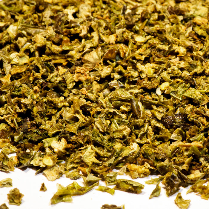 Close-up of Whole Spice Inc. Jalapeño Green Chili Diced scattered on a white surface, showing small, irregular pieces in vibrant green and yellow-green hues.