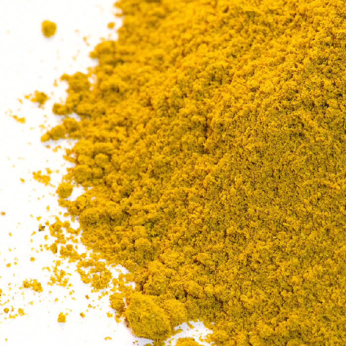 A close-up of Whole Spice Inc.'s Japanese Curry powder, its bright yellow color scattered on a white surface—ideal for creating aromatic coconut curry sauce or flavorful Japanese curry dishes.