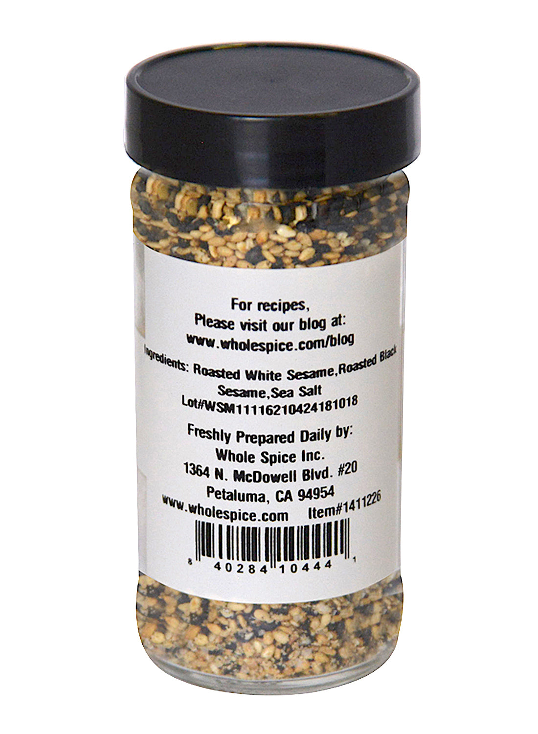 A clear spice jar with a black lid contains Japanese Gomashio by Whole Spice Inc., a roasted sesame salt blend of white and black sesame seeds with sea salt. The label lists ingredients, preparation details, company info, website, and address.