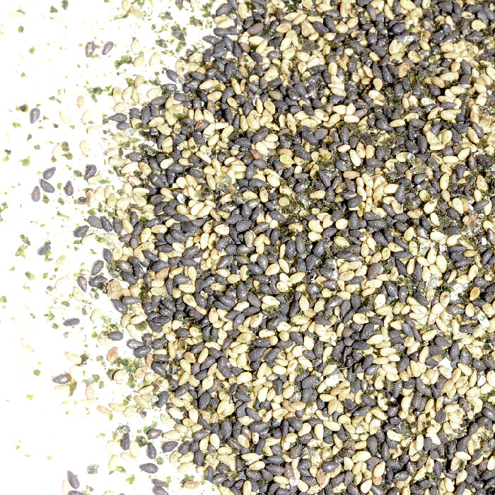 A close-up of Whole Spice Inc.'s Japanese Seaweed Rice Seasoning - Sweet & Salty, featuring black and white sesame seeds with green seaweed flakes scattered on a white surface.