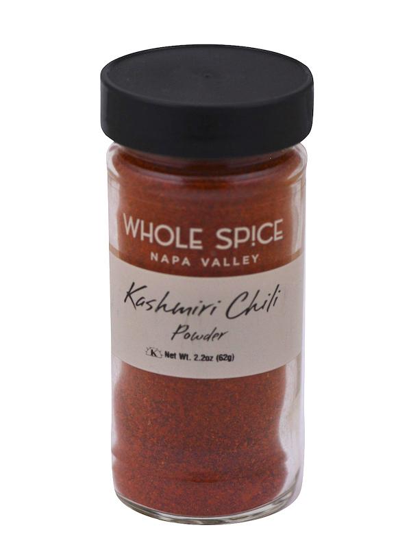 A glass jar of Whole Spice Inc. Kashmiri Chili Powder with a black lid and beige label shows the product name and weight. Inside, the vibrant red chili powder is prized in Indian cuisine for its color and flavor.