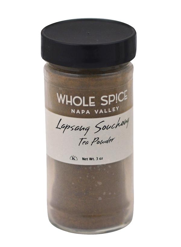 A clear glass jar with a black lid labeled Whole Spice Inc. Lapsang Souchong Tea Powder, holding 3 oz of brown tea powder known for its smoky flavor and pine aroma.