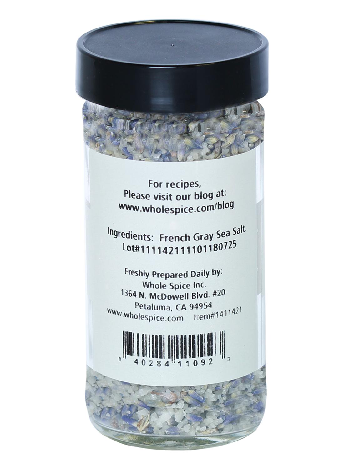 A clear glass jar with a black lid from Whole Spice Inc. contains Lavender Salt. A white label lists details, while the salt inside shows gray and purple hues, evoking the delicate appearance of lavender sea salt.