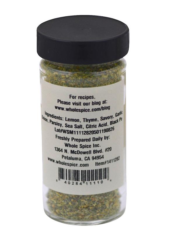 A clear spice jar with a black lid from Whole Spice Inc. holds Lemon Herb Seasoning, a yellow-green blend with lemon, thyme, and parsley—ideal for fish and chicken—with the producer’s contact info on the label.
