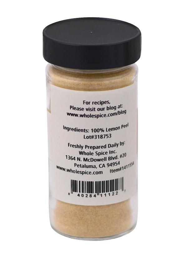 A clear spice jar with a black lid contains yellow Lemon Peel Powder from Whole Spice Inc.; the back label states the ingredient as 100% ground lemon peel, lists manufacturer details, and gives a website for baking recipes.