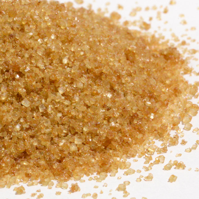 A close-up of Whole Spice Inc. Lemon Sugar crystals on a white surface, highlighting their coarse texture and golden-brown color.