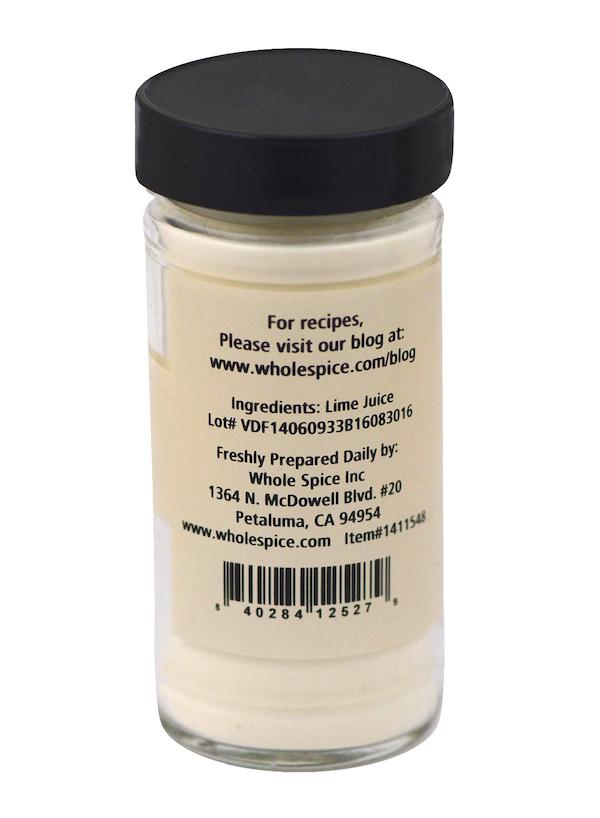 A clear spice jar with a black lid contains white Lime Juice Powder by Whole Spice Inc.; the back label lists lime juice as an ingredient, includes brand contact and location, and recommends it as a substitute for lime juice.