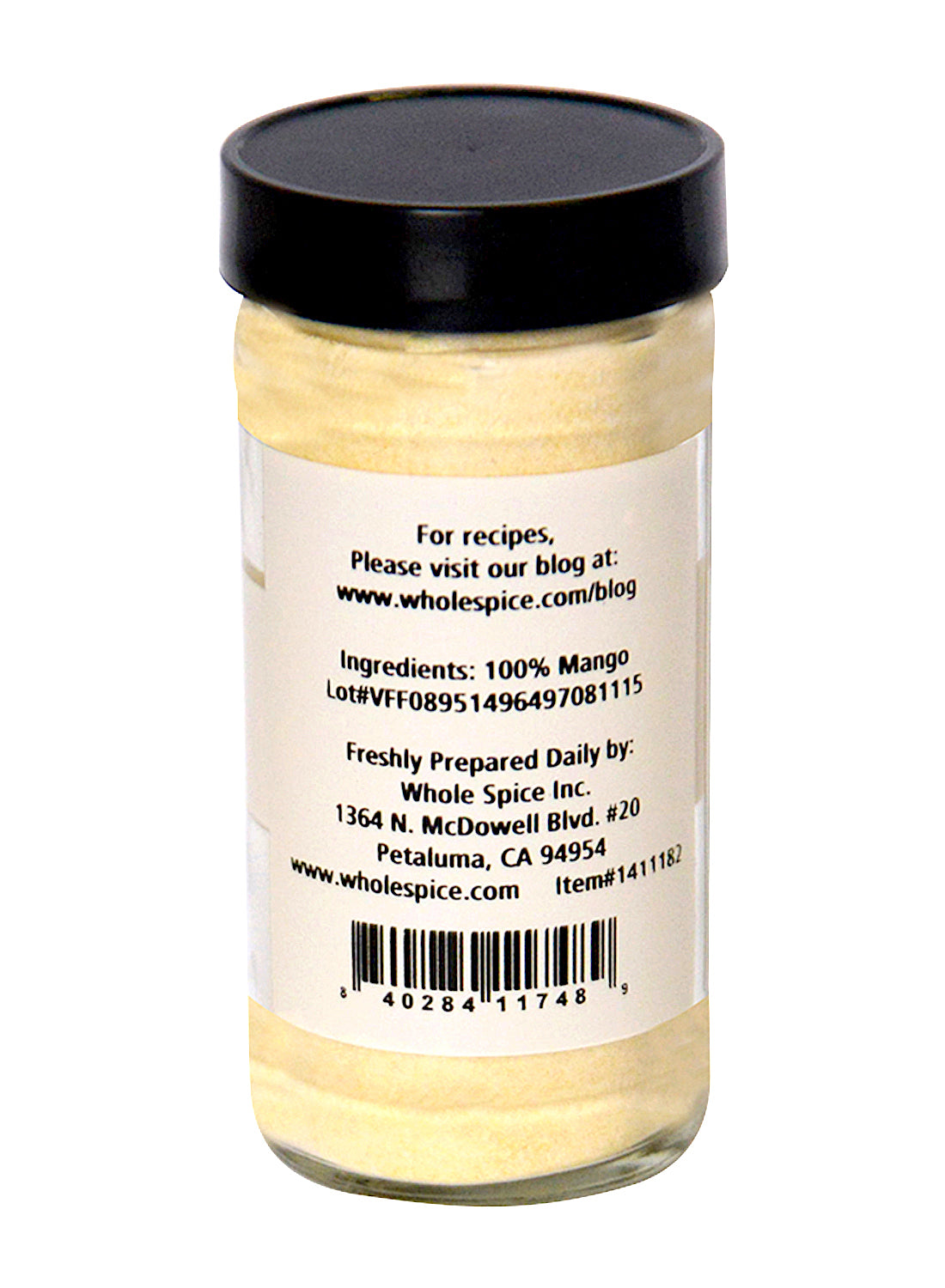 A clear spice jar with a black lid holds vibrant yellow Mango Fruit Powder by Whole Spice Inc. The label states 100% mango and includes the website, address, lot, and item numbers for the Petaluma, CA-based brand.