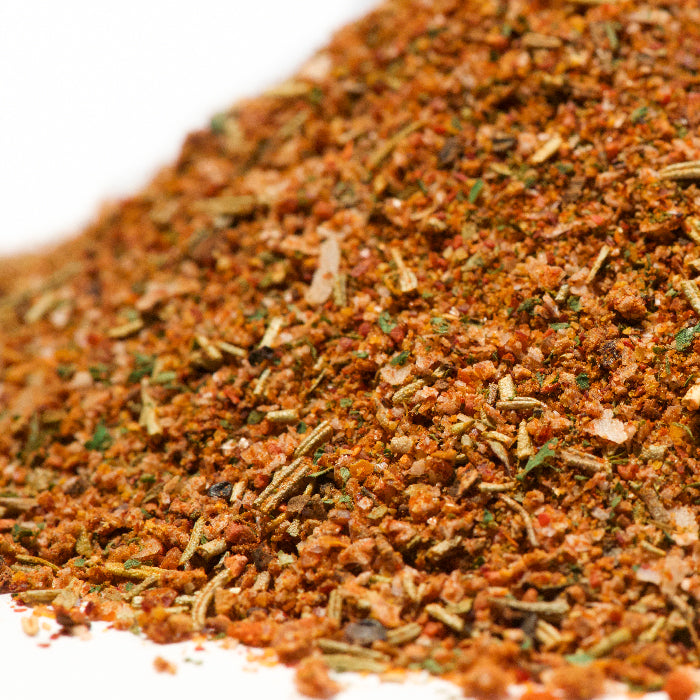 A close-up of a pile of Mediterranean Roasting Rub by Whole Spice Inc., highlighting its vibrant textures and colors, mixed with kosher salt and displayed on a clean white background.