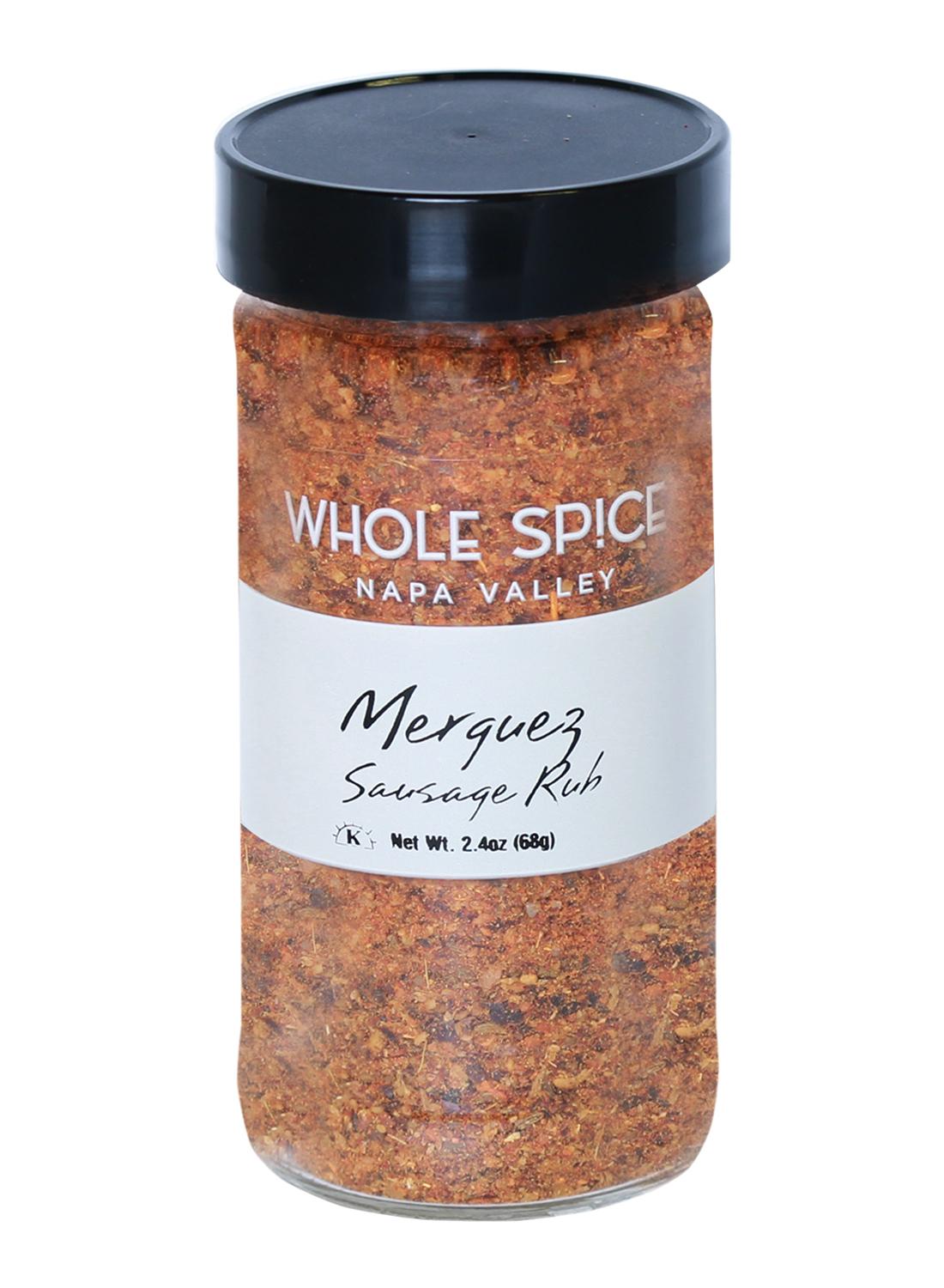A clear 2.4 oz (68g) spice jar from Whole Spice Inc. labeled Merguez Sausage Rub, featuring a black lid and containing a reddish-brown Moroccan-inspired seasoning blend.