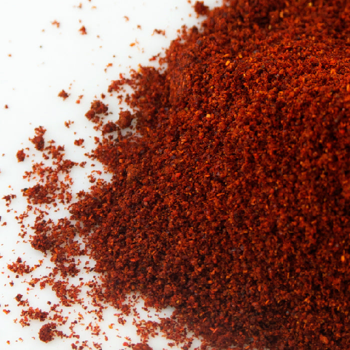 A close-up of Whole Spice Inc.'s Moroccan Paprika & Olive Oil, featuring finely ground paprika scattered on a white surface, highlights its vibrant red hue and gourmet appeal.