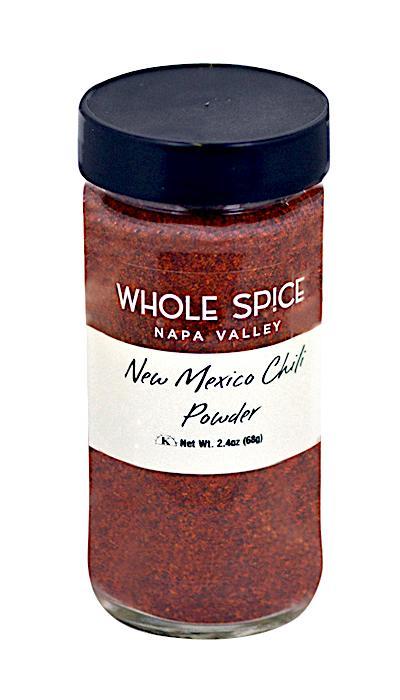 A clear glass jar labeled Whole Spice Inc. New Mexico Chili Powder with a black lid holds 2.4 oz (68g) of reddish-brown chili powder, ideal for Mexican dishes.