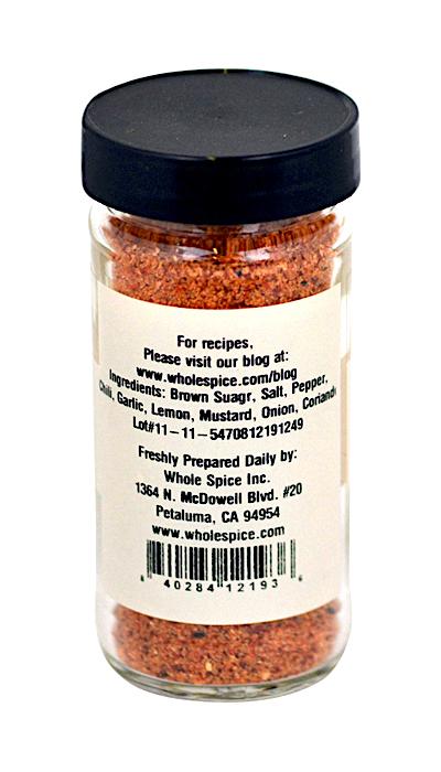 A clear glass jar with a black lid displays Whole Spice Inc.’s Northwest Salmon Rub, a reddish-brown fish seasoning. The label shows ingredients, contact info, and a website for cedar plank salmon recipes from Petaluma, CA.