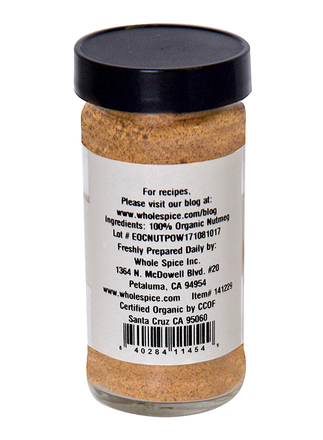 A clear spice jar with a black lid shows a label for Nutmeg Powder Organic by Whole Spice Inc., listing 100% organic nutmeg, recipe blog directions, and company info from Petaluma, CA.