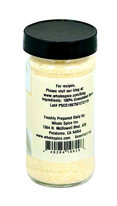 A clear spice jar with a black lid holds light yellow Onion Granulated by Whole Spice Inc. The label states it's 100% dehydrated onion, with barcode, address, and website provided for more details.