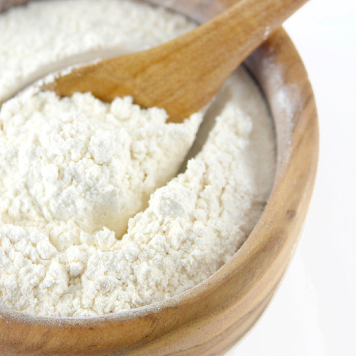 A wooden bowl of white flour with a spoon and loose flour on the rim—perfect for cooking with Whole Spice Inc. Onion Powder, ready to enhance recipes with savory onion flavor.