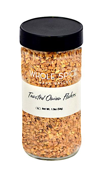 A clear glass jar with a black lid holds Whole Spice Inc. Onion Toasted Flakes, Net Wt. 1.9oz (54g)—ideal for soup bases and seasonings.