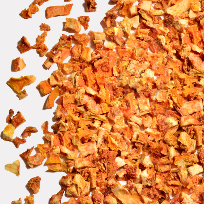 A close-up of Whole Spice Inc. Orange Peels shows dried, diced pieces in various sizes, scattered on a light gray surface. They display shades of orange and light brown, offering a hint of citrus flavor.