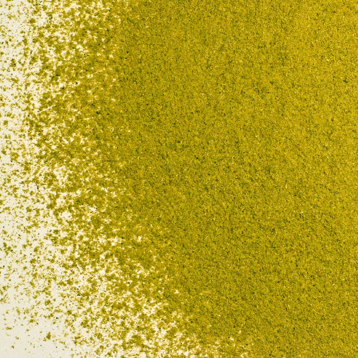 A pile of Whole Spice Inc. Oregano Powder Organic is spread unevenly on a white surface, forming a textured green-yellow gradient from dense to sparse particles on the left side.