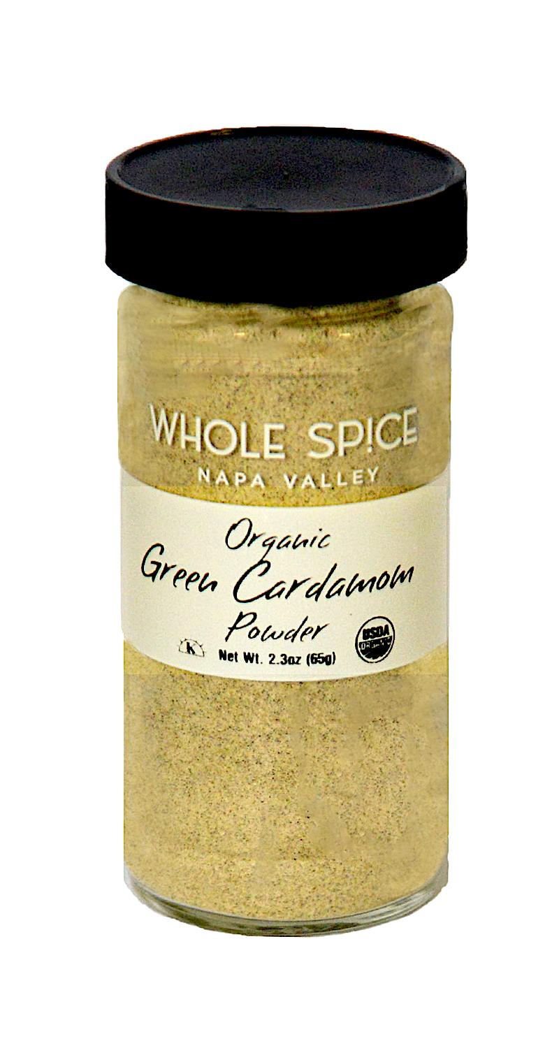 A glass jar with black lid labeled "Whole Spice Inc. Green Cardamom Powder Organic" contains light green ground cardamom, net weight 2.3oz (65g), and features organic certification logos.