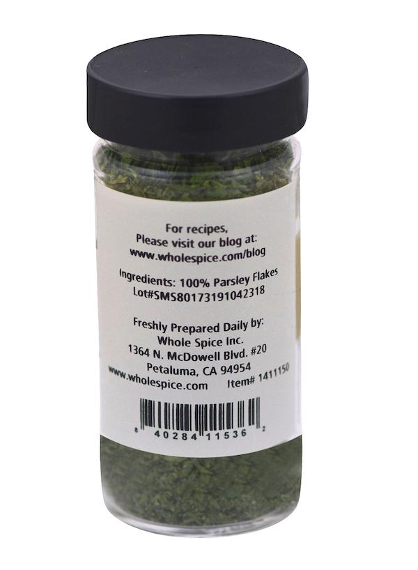 A clear spice jar with a black lid from Whole Spice Inc. contains 100% Parsley Flakes. The dried herb makes a great garnish or ingredient and the label includes company and contact details.
