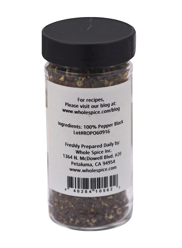 A clear spice jar with a black lid holds Whole Spice Inc. Pepper Black Cracked. The label lists the ingredient as 100% black pepper and includes the manufacturer’s address, website, and a barcode.