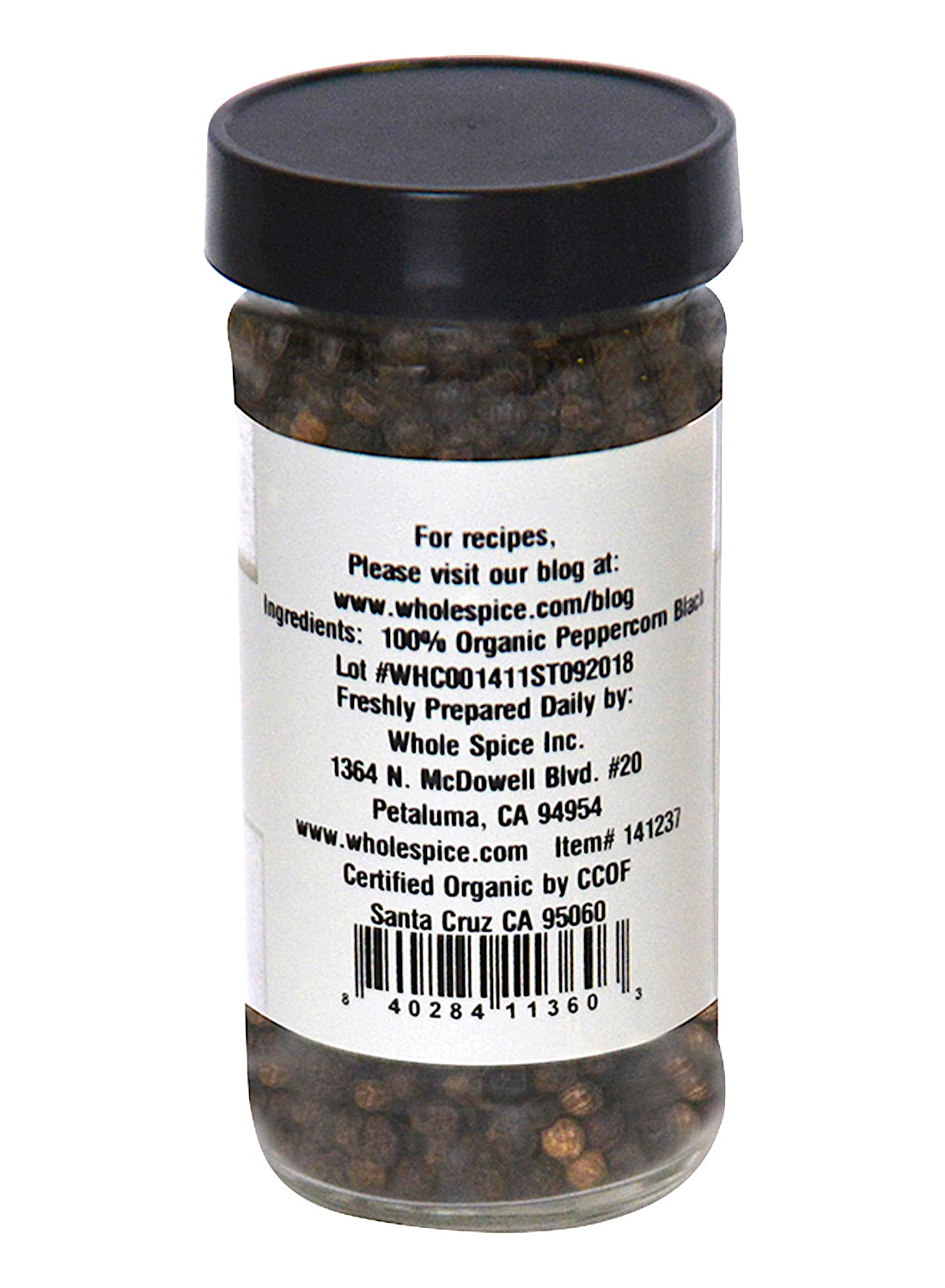 A glass jar with a black lid holds Whole Spice Inc. Peppercorns Black 100% Organic, the King of Spices. The label lists ingredients, preparation tips, a recipe website, and features a barcode at the bottom.