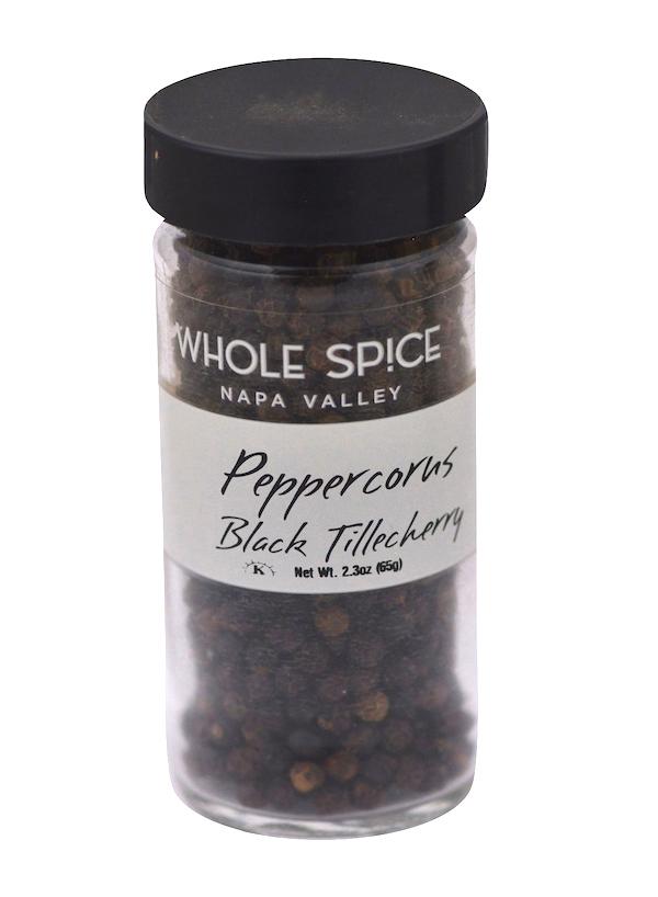 A clear glass jar with a black lid, labeled Whole Spice Inc. Peppercorns Black Tellicherry, contains premium whole black peppercorns from the Malabar Coast.