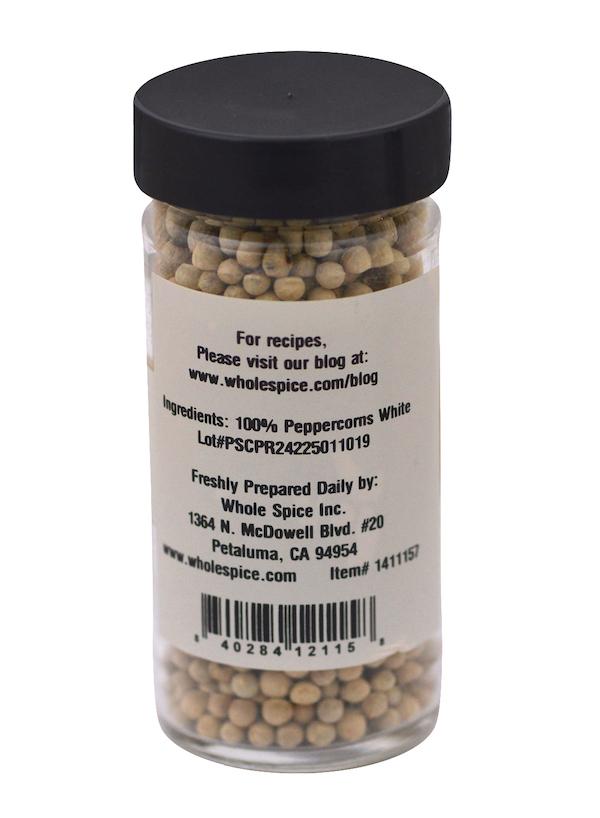 A clear jar of Whole Spice Inc. Peppercorns White, filled with 100% white peppercorns and sealed with a black lid—ideal for seasoning white sauces. Label includes company info and contact details.