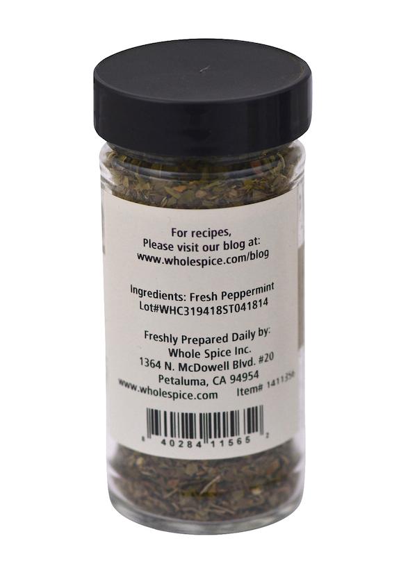 A clear spice jar from Whole Spice Inc., labeled "Peppermint Leaves," features a black lid and displays dried spearmint inside. The label details ingredients, company info, and a website for mint recipes.