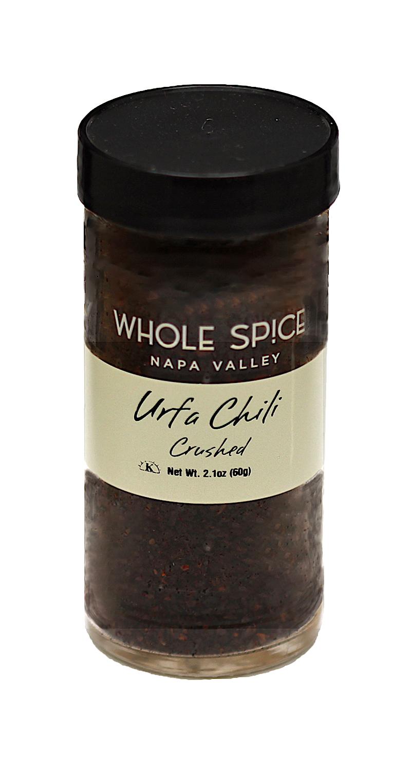 A clear spice jar with a black lid labeled Whole Spice Inc. Urfa Chili Crushed, filled with dark Turkish chili flakes (Isot pepper). Net weight: 2.1 oz (60g).