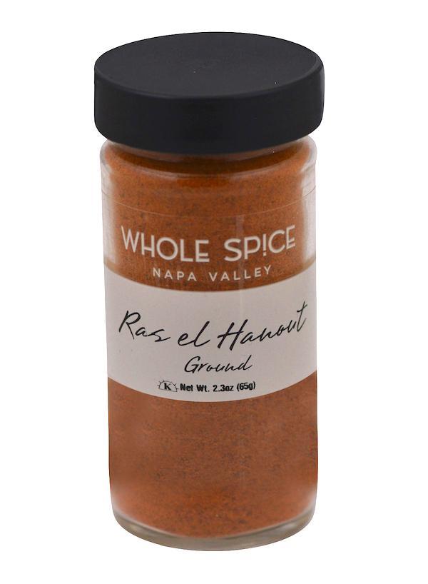 A 2.3 oz (65g) glass jar of Whole Spice Inc. Ras el Hanout Ground, an aromatic Moroccan blend, with a black lid, white label, and reddish-orange spice inside.