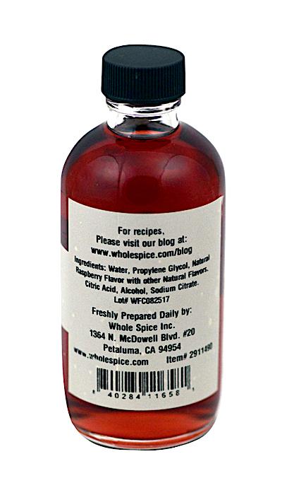 A clear bottle with a black cap contains red liquid. The back label has ingredients, contact info, and a barcode. It’s Raspberry Extract from Whole Spice Inc.