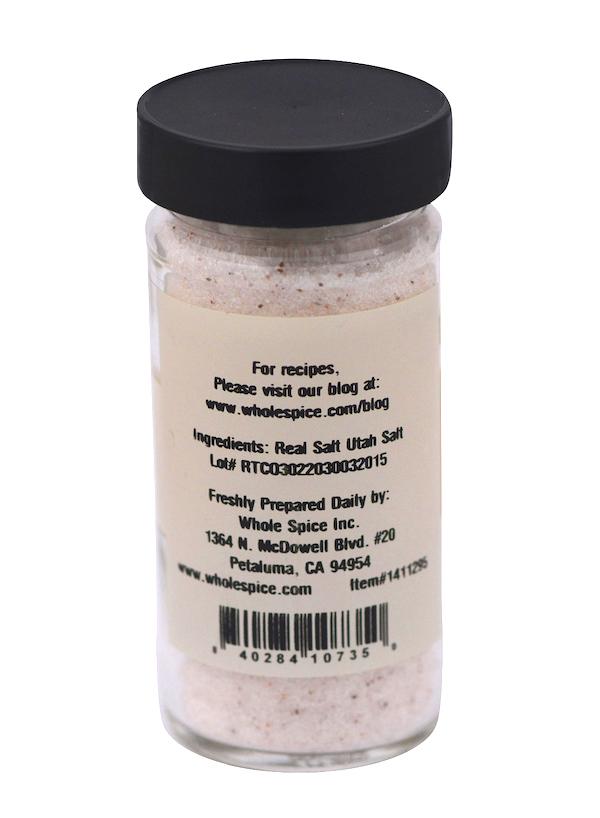 A clear spice jar with a black lid holds Real Utah Salt Fine by Whole Spice Inc., rich in trace minerals. The label lists ancient sea salt as the ingredient, plus the maker's address, recipe website, and barcode at the bottom.