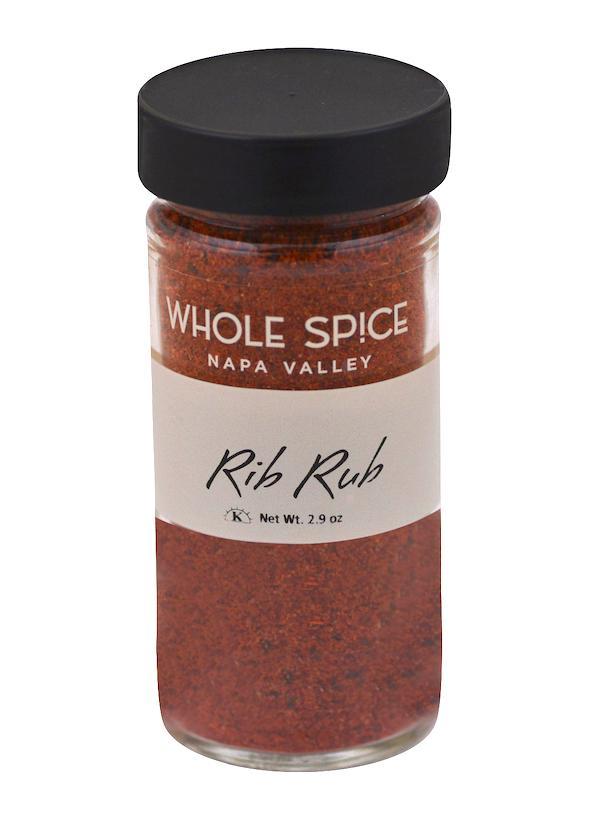 A clear glass jar with a black lid holds Whole Spice Inc. Rib Rub seasoning. The white label with black and orange text shows the name, 2.9 oz net weight, and promotes its bold barbecue flavor for perfect grilling.