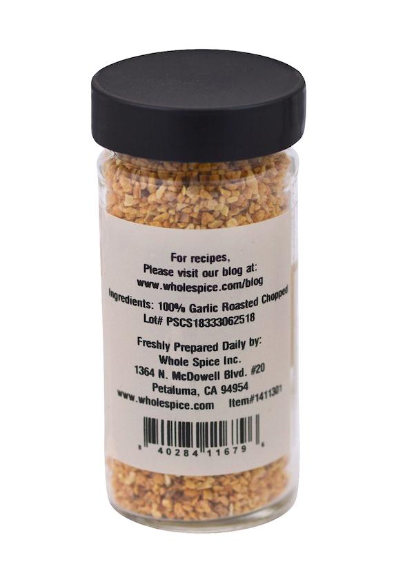 A clear jar labeled "Garlic Roasted Chopped" by Whole Spice Inc., with a black lid, holds chopped roasted garlic granules—ideal for Mediterranean cuisine. The label shows 100% garlic, company details, location, and a bottom barcode.