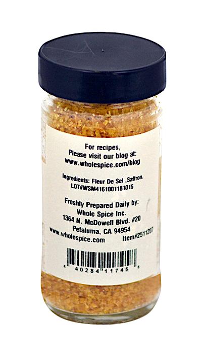 Saffron Salt by Whole Spice Inc. comes in a glass jar with a black lid, featuring a yellow-orange blend of fleur de sel and saffron. The label includes ingredients, contact info, and a recipe website.