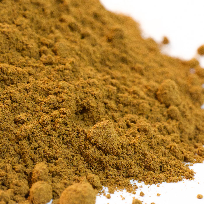 A close-up of Whole Spice Inc. Cinnamon Powder on a white surface highlights its fine, crumbly texture and small clumps—a premium spice made from aromatic Cassia cinnamon.