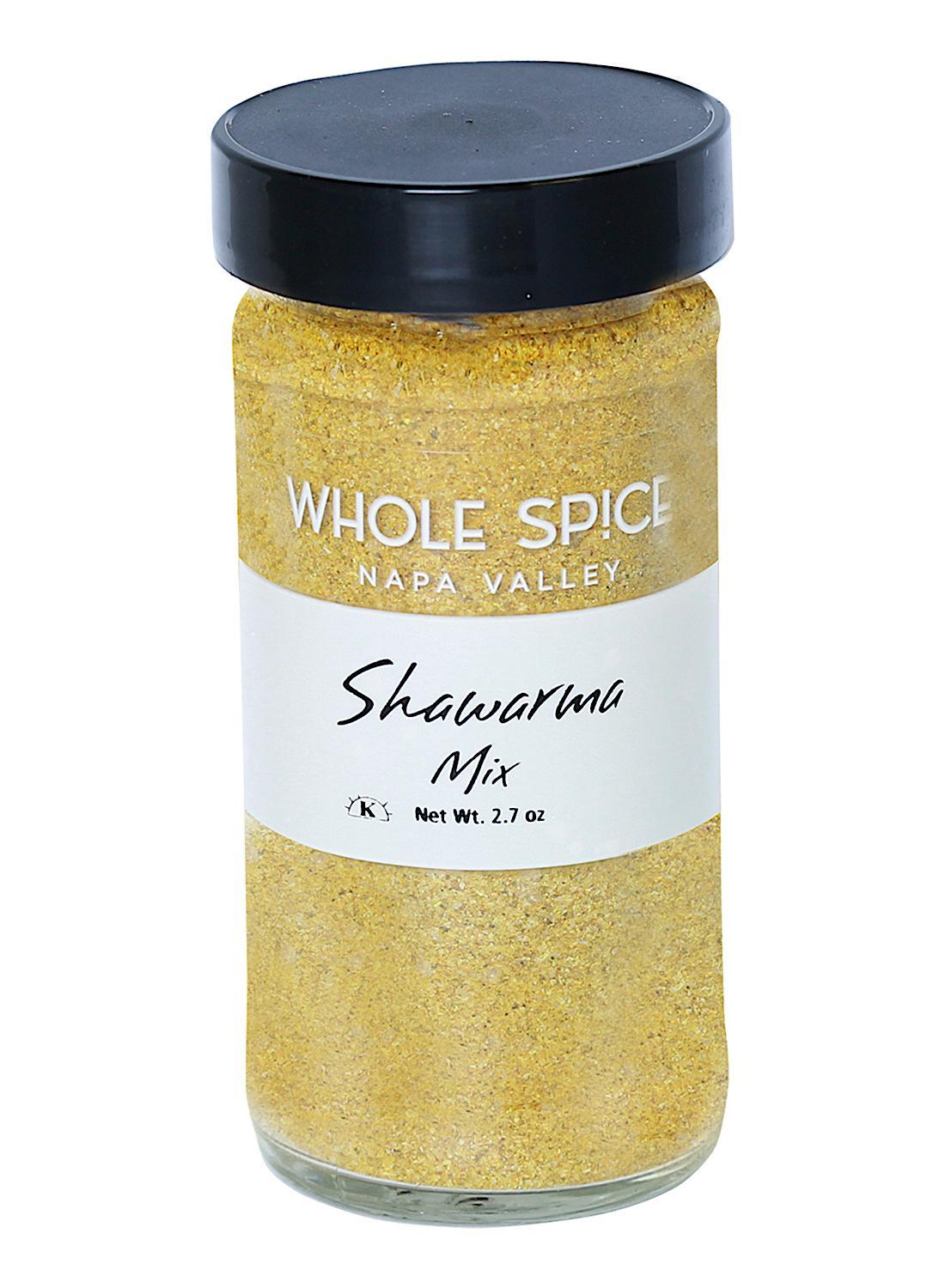 A clear glass jar with a black lid contains yellowish Shawarma Spice Mix by Whole Spice Inc., Net Wt. 2.7 oz.