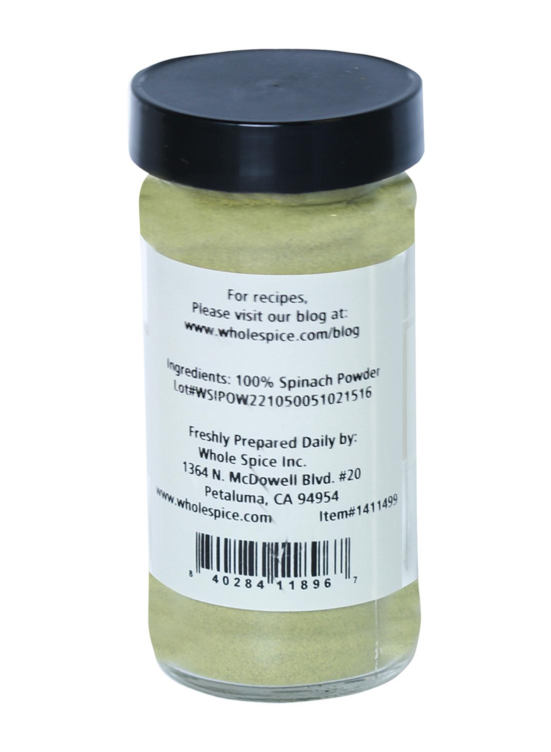 A clear spice jar with a black lid contains vibrant Spinach Powder. The label shows 100% spinach powder and lists Whole Spice Inc., Petaluma, CA, along with company contact details and website.