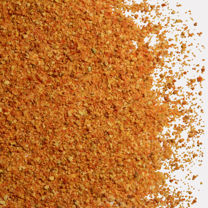 A close-up of Whole Spice Inc. Tangerine Peel seasoning, featuring orange and yellow dehydrated tangerine peel with coarse and fine granules, scattered across a white surface.